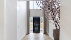 A hallway with a wooden herringbone floor, a large potted plant, and a black door leading outside. - Beautiful Water Villa Near Harderwijk (Zeewolde)
