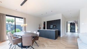A modern kitchen with a central island, a dining area with a round table and chairs, and a living area with a sofa. - Beautiful Water Villa Near Harderwijk (Zeewolde)