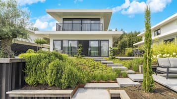 A modern two-story house with a balcony, surrounded by well-maintained gardens and a wooden deck.