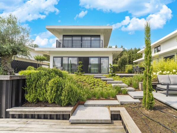 A modern two-story house with a balcony, surrounded by well-maintained gardens and a wooden deck.