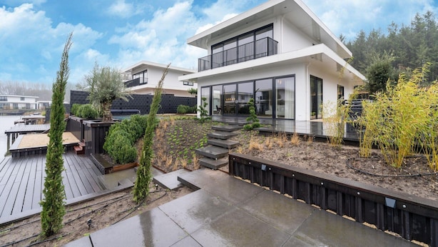 A modern two-story house with a balcony, a wooden deck, and a garden area. - Beautiful Water Villa Near Harderwijk (Zeewolde)