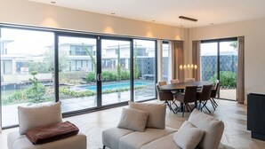 A spacious living room with a large window, a dining area, and a pool view. - Beautiful Water Villa Near Harderwijk (Zeewolde)