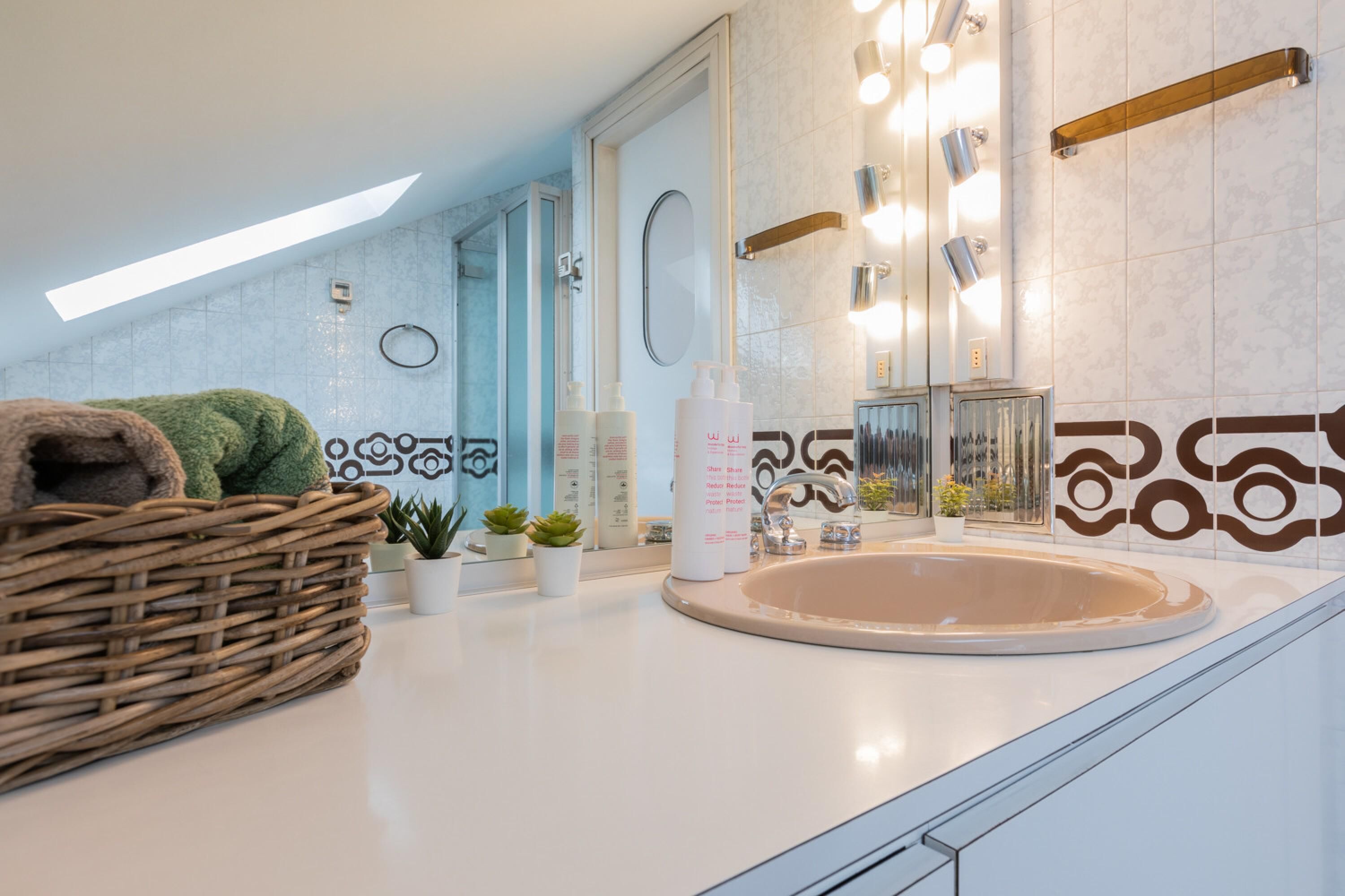 A modern bathroom with a large mirror, a round sink, and a skylight.