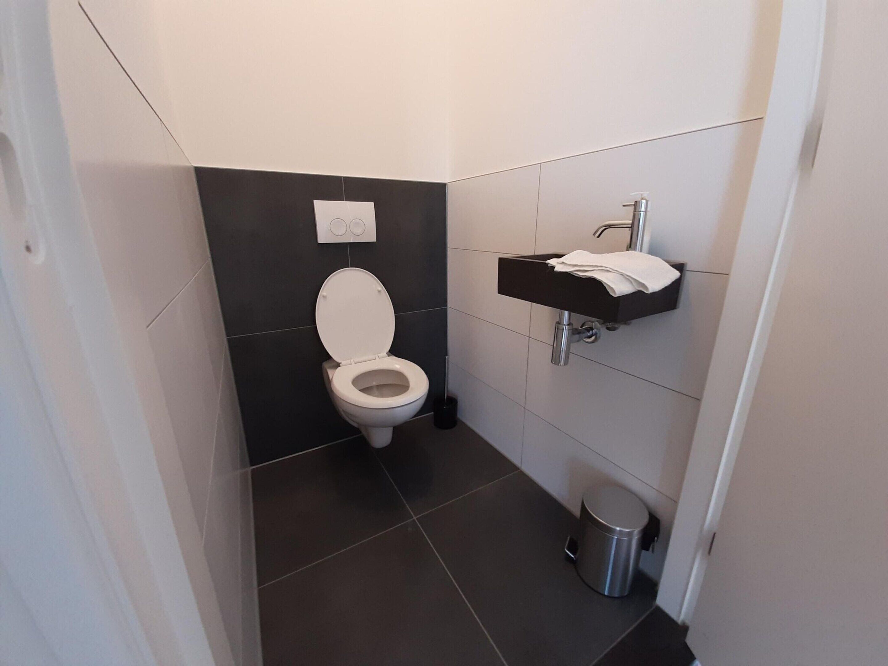 Een moderne badkamer met toilet, wastafel en prullenbak.