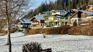 A snow-covered landscape with a row of multi-story buildings, likely a ski resort or mountain lodge, featuring balconies and large windows. - Nice Apartment in Hopfen am See (Fuessen)