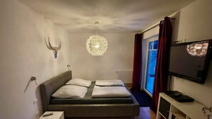 A bedroom with a bed, a bedside table, a TV, a ceiling light, and a window with curtains. - Nice Apartment in Hopfen am See (Fuessen)