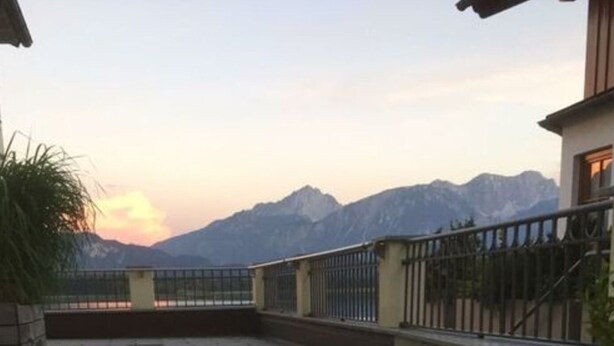 A wooden table with two glasses of a clear liquid, possibly water or wine, on a patio with a view of mountains in the background. - Nice Apartment in Hopfen am See (Fuessen)