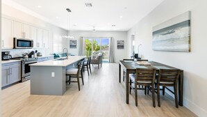 Una cocina moderna con una isla central, comedor con sillas de madera y vistas al exterior.