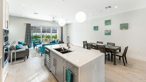 Una cocina moderna con una isla central, comedor con sillas de madera y sala de estar con sofá y sillones.