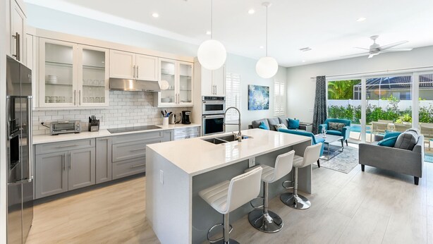 Una cocina moderna con una isla central, taburetes de bar y una zona de comedor con sofá y sillas.