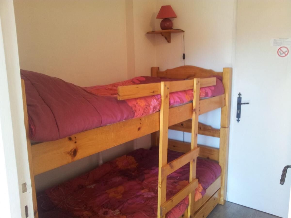 A bunk bed with a red blanket and a small shelf with a lamp.