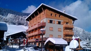 A multi-story wooden building with balconies, surrounded by snow-covered trees and a clear sky.