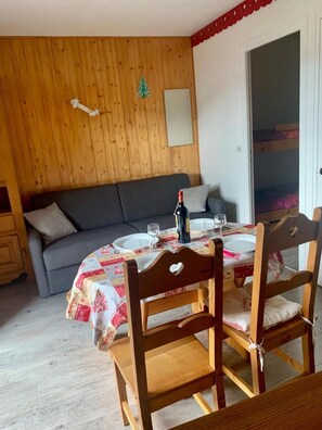 A cozy dining area with a wooden table set for two, a grey sofa, and a wooden cabinet. - 300m from resort center, 2nd floor, balcony, parking, tv, ski locker, 23m², Les Gets (Les Gets)