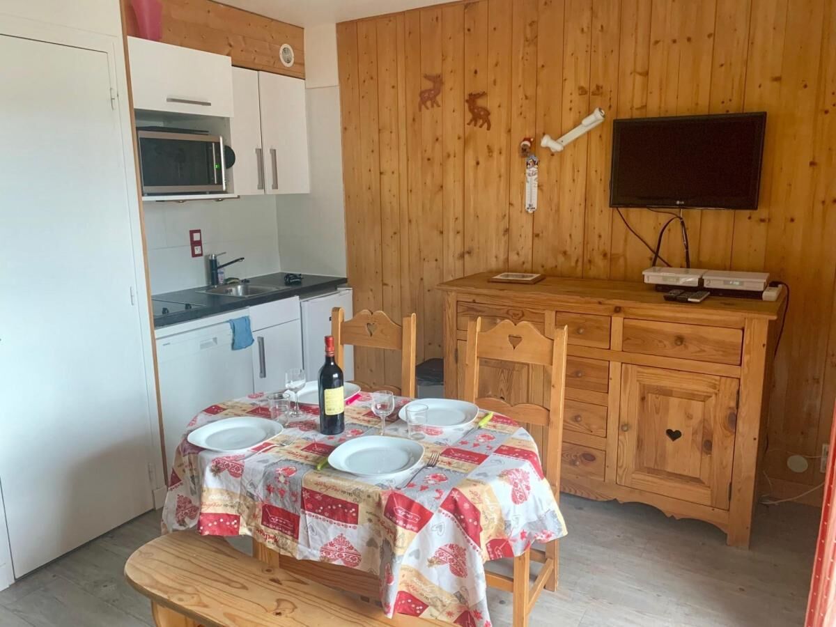 A dining area with a table set for four, a bottle of wine, and a television on a wooden cabinet.
