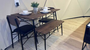 Une pièce aménagée comme une tente, avec une table en bois dressée pour le repas, des chaises noires et un banc.