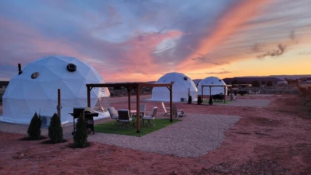 Des dômes géodésiques dotés d’un espace extérieur aménagé et d’une zone couverte, le tout se dressant sur fond de ciel au coucher du soleil.