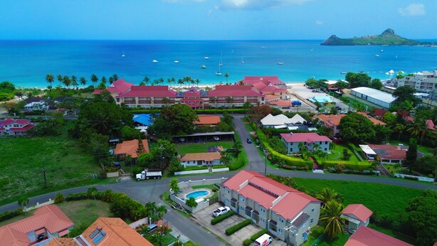 An aerial view of a coastal resort with multiple buildings, a swimming pool, and a view of the ocean with boats. - Nestled in Rodney Bay: Steps from Beaches, Shops, and Dining in St. Lucia. (Rodney Bay)