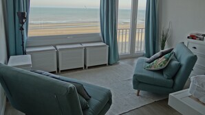 A living room with a view of the beach, a sofa, a small table, and a white cabinet. - Apartment in Nieuwpoort With Stunning Sea View (Nieuwpoort)