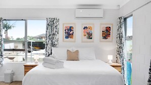 Une chambre d’hôtel moderne avec un grand lit, une vue sur l’extérieur et trois œuvres d’art encadrées accrochées au mur.