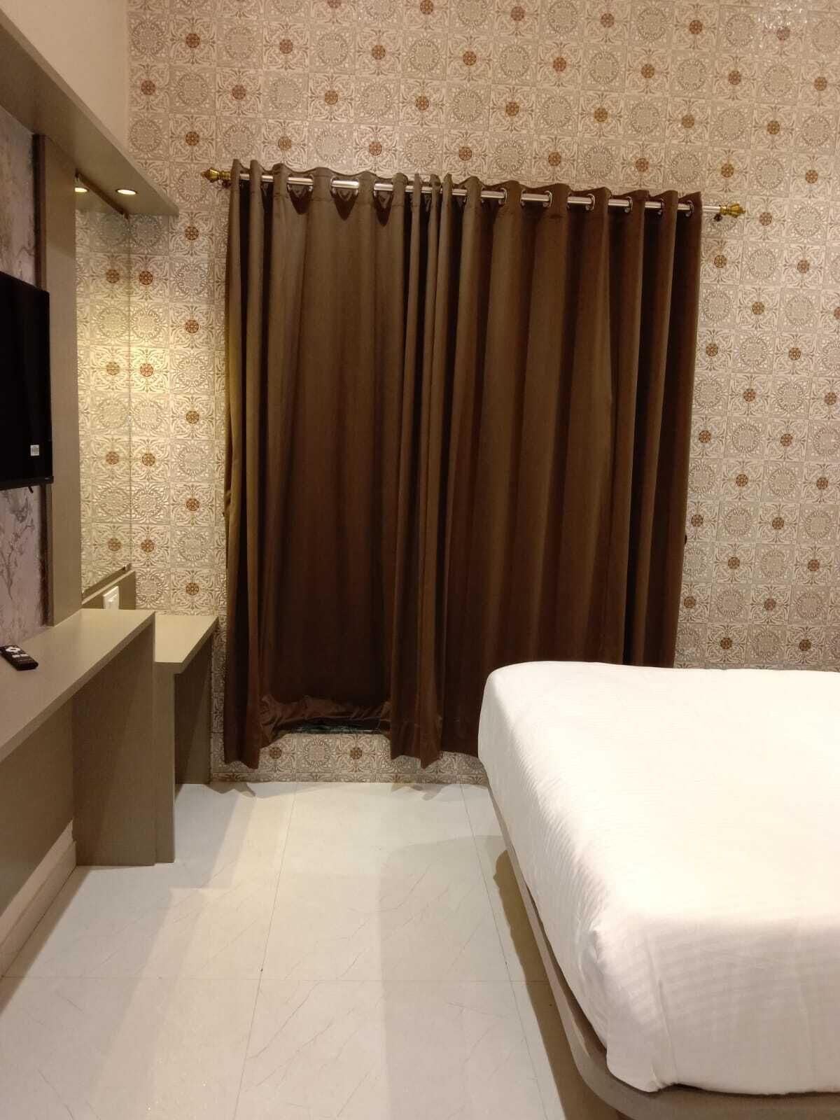 A hotel room with a bed, a bedside table, a mirror, and a curtain.