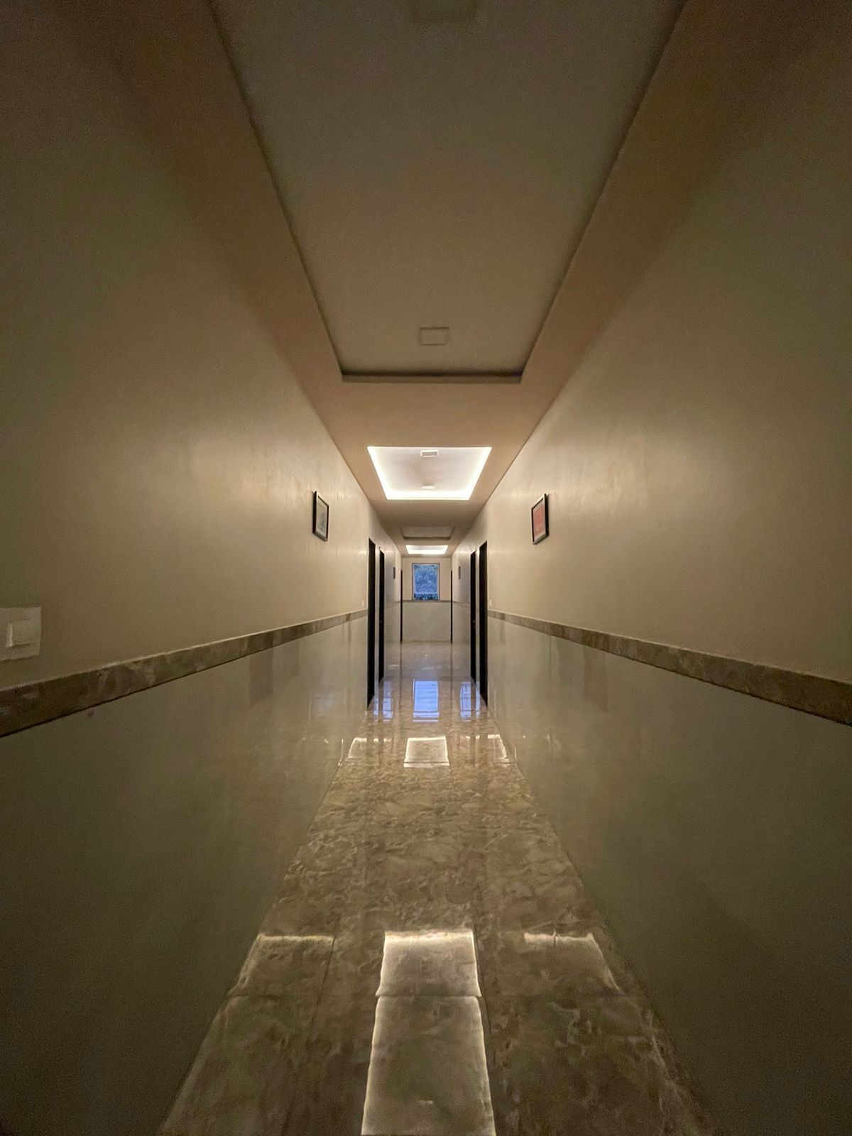 Un largo y estrecho pasillo con suelo de mármol pulido e iluminación empotrada.