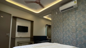 A modern hotel room with a bed, ceiling fan, air conditioning unit, and a flat-screen TV. - JP GARDEN & LAWN (Mumbai)