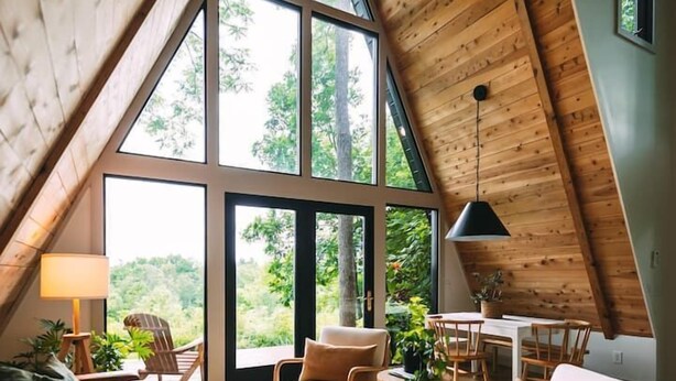 A cozy, high-ceilinged room with a large window, wooden furniture, and a dining area. - JP GARDEN & LAWN (Mumbai)