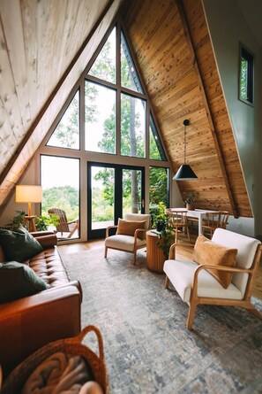 A cozy, high-ceilinged room with a large window, wooden furniture, and a dining area. - JP GARDEN & LAWN (Mumbai)