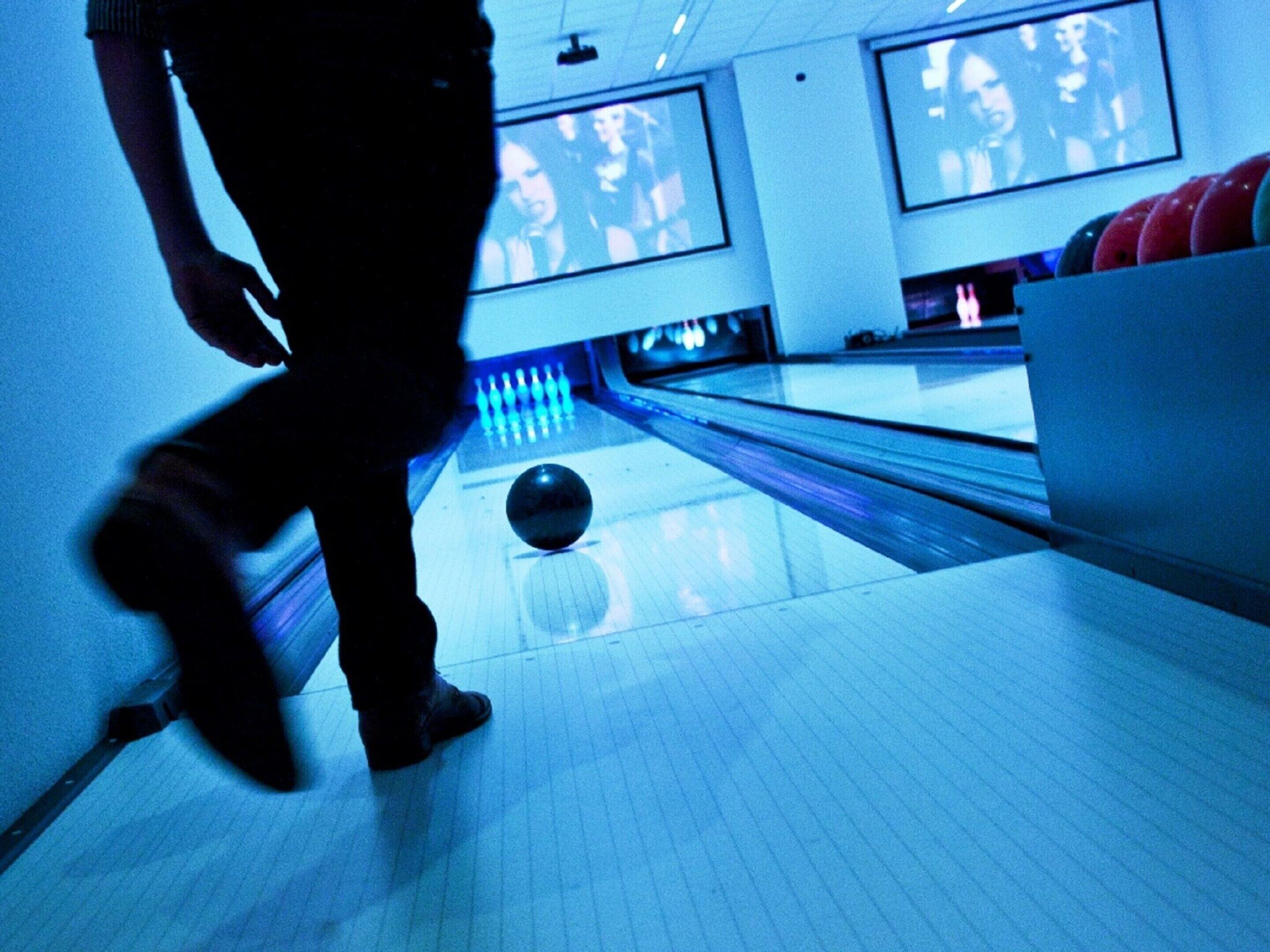 Een bowlinghal met banen, kegels en een bowlingbal in beweging.