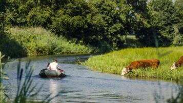 A river with a boat carrying people and cows grazing on the bank.