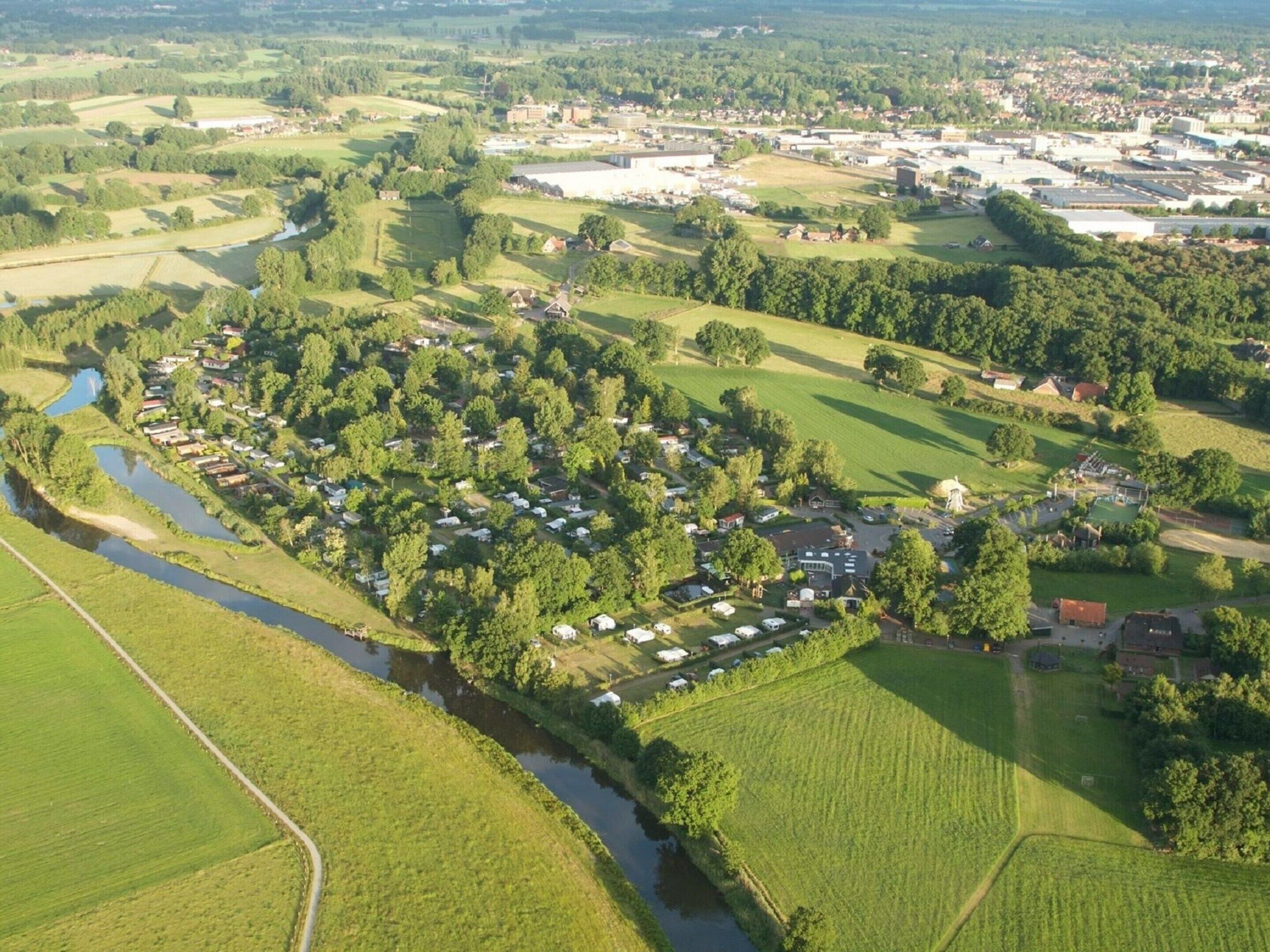 An aerial view of a rural area with a river, green fields, and a cluster of mobile homes.