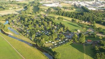 An aerial view of a rural area with a river, green fields, and a cluster of mobile homes.