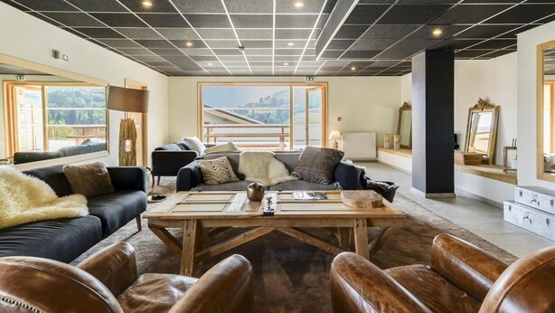 A spacious lounge area with leather seating, a wooden coffee table, and a large window offering a view of the outdoors. - Wifi, 200m from resort center, view mountain, swimming pool, sauna, hammam, terrace, balcony, tv (Combloux)