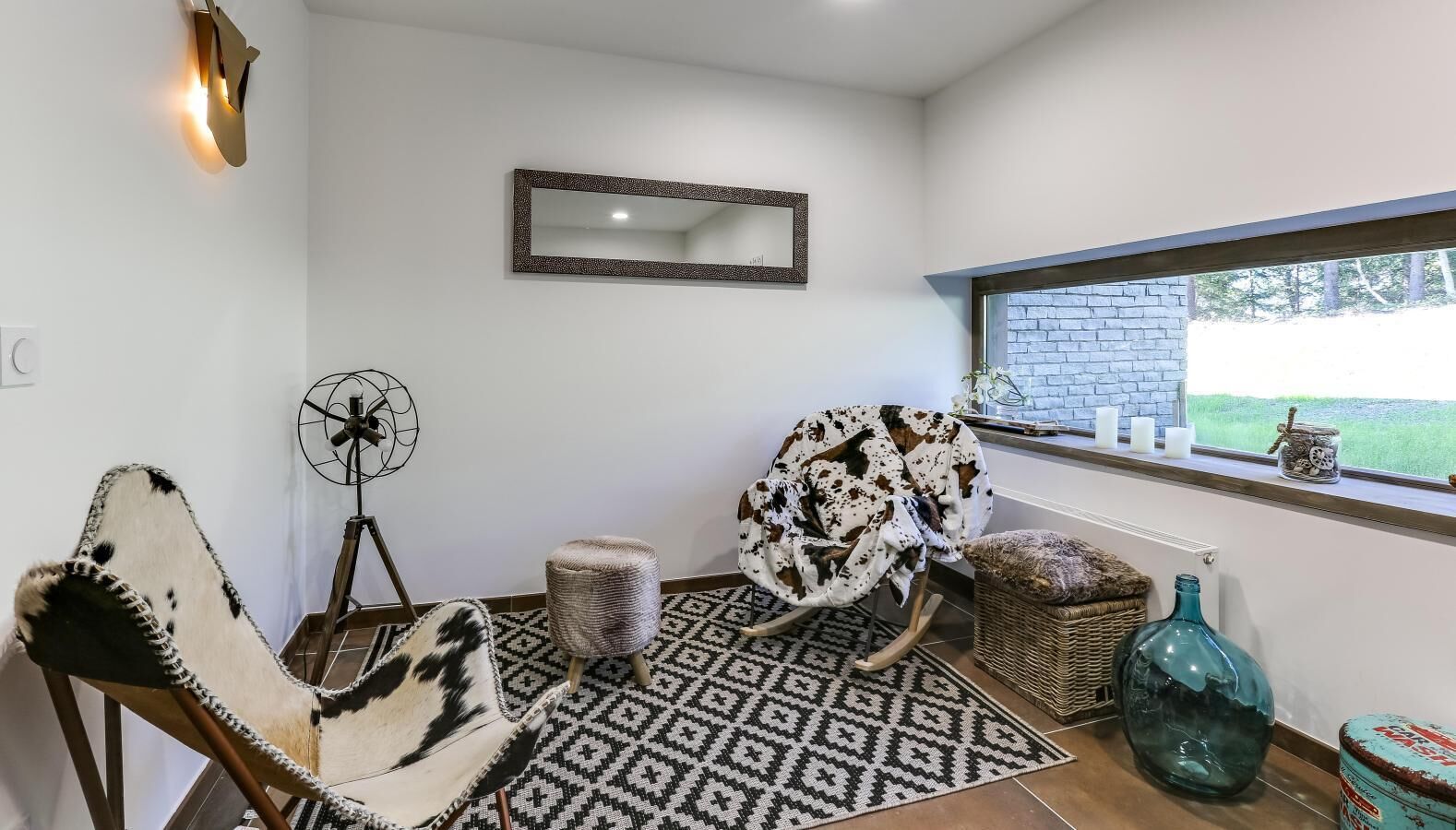 Ein Zimmer mit zwei Schaukelstühlen, einem Ventilator, einem gemusterten Teppich, einem Fenster mit Blick und einem Spiegel an der Wand.