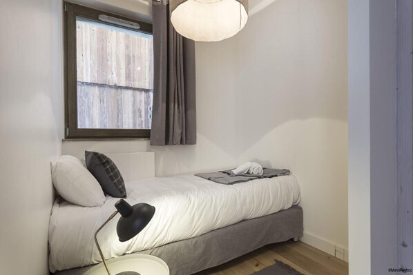 A small, neatly arranged bedroom with a bed, bedside lamp, and a window with curtains.