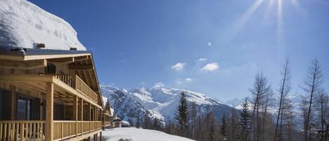 A wooden lodge with a balcony overlooking a snowy mountain landscape.