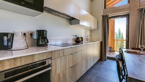 A modern kitchen with a microwave, coffee maker, and toaster. There is a wooden dining table with chairs and a view of the outdoors. - Wifi, sauna, terrace, balcony, parking, tv, ski locker, 79m², La Rosière (La Rosière Montvalezan)