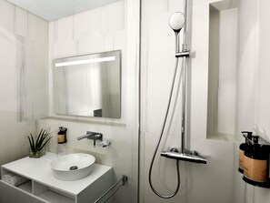Une salle de bain moderne avec un lavabo blanc, un grand miroir, une douchette à main et un porte-serviettes.