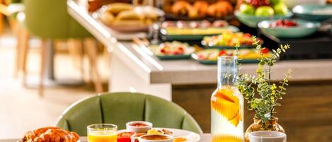 Una mesa de desayuno con platos de comida, un vaso de jugo de naranja y una taza con una bolsita de té.