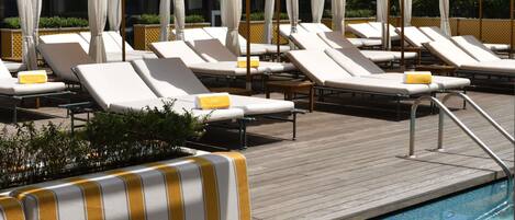 Un espace aménagé au bord de la piscine, avec des chaises longues, des parasols à rayures jaunes et une terrasse en bois.