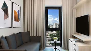 Una moderna camera d'hotel con un divano, un tavolino con un vaso, una TV a schermo piatto e una finestra vista città.