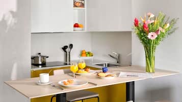Una cocina moderna con una mesa de comedor, sillas, un jarrón de flores y un frutero.