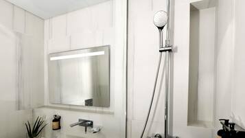 Ein modernes Badezimmer mit Waschbecken, großem Spiegel, Handbrause und Handtuchhalter.