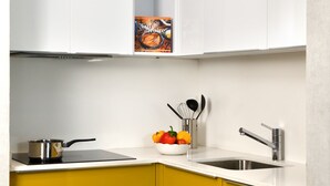 A compact kitchen with white upper cabinets, a yellow lower cabinet, a stove, a sink, and a bowl of fruit on the counter. - Aparthotel Adagio Abidjan Marcory (Abidjan)