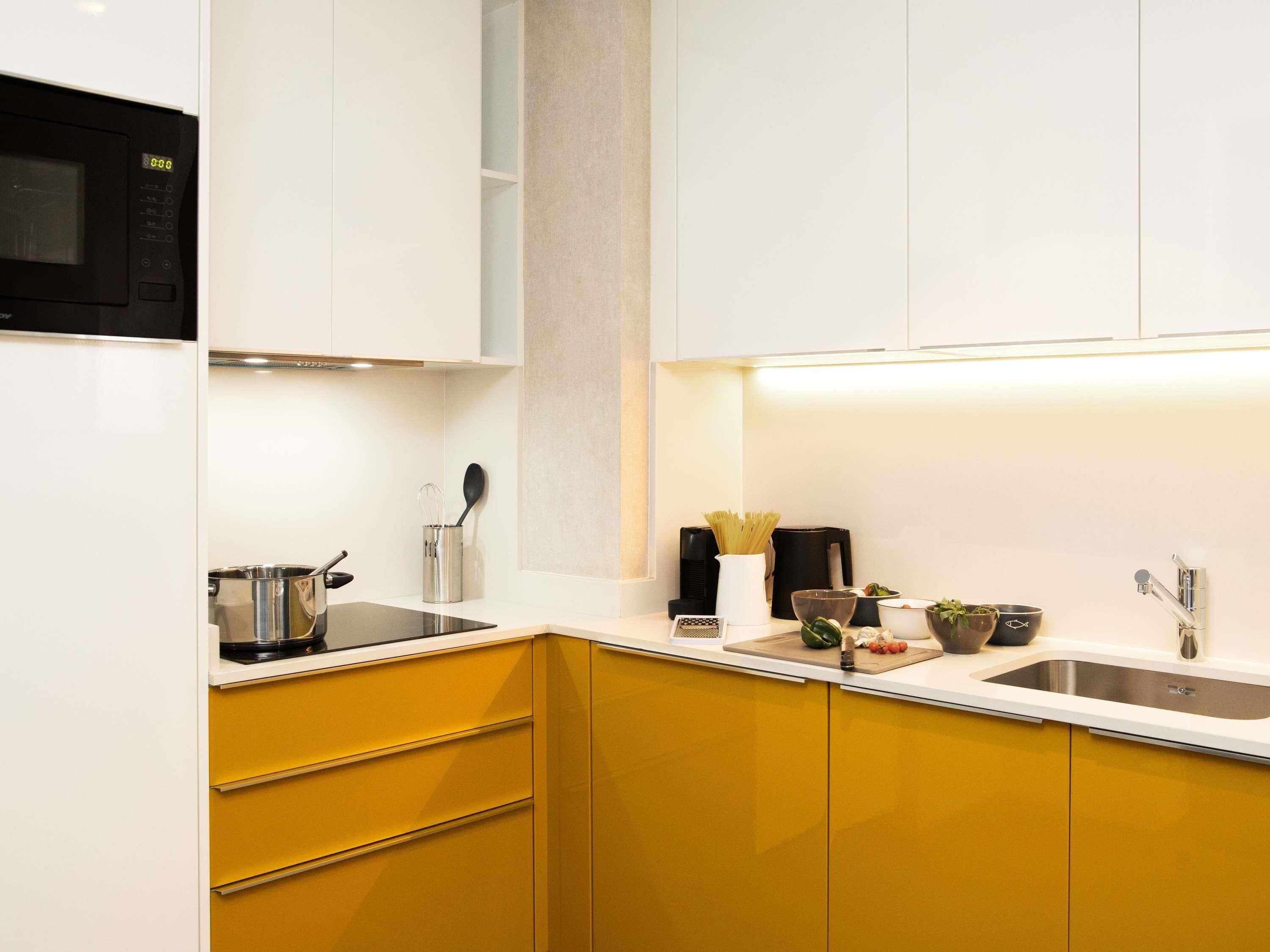 A modern kitchen with white cabinets, a yellow countertop, a black microwave, and stainless steel appliances.