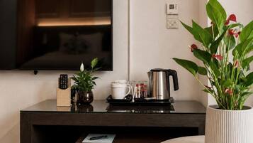 Una habitación moderna con una televisión de pantalla plana montada en la pared, una cafetera, una planta y un control remoto sobre una mesa de madera.