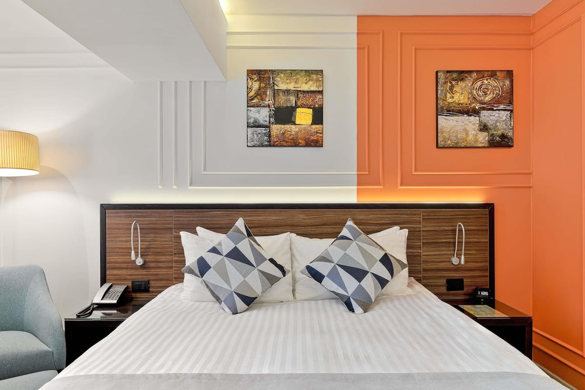 Une chambre d’hôtel avec un lit, deux tables de chevet, une lampe et des œuvres d’art accrochées aux murs.