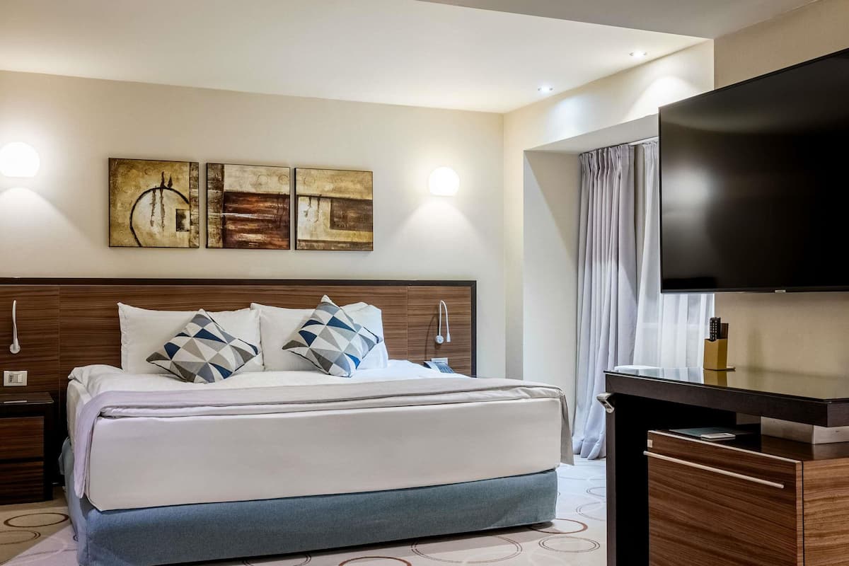 Une chambre d’hôtel équipée d’un lit, d’un téléviseur à écran plat, d’œuvres d’art au mur et d’un bureau avec un miroir.