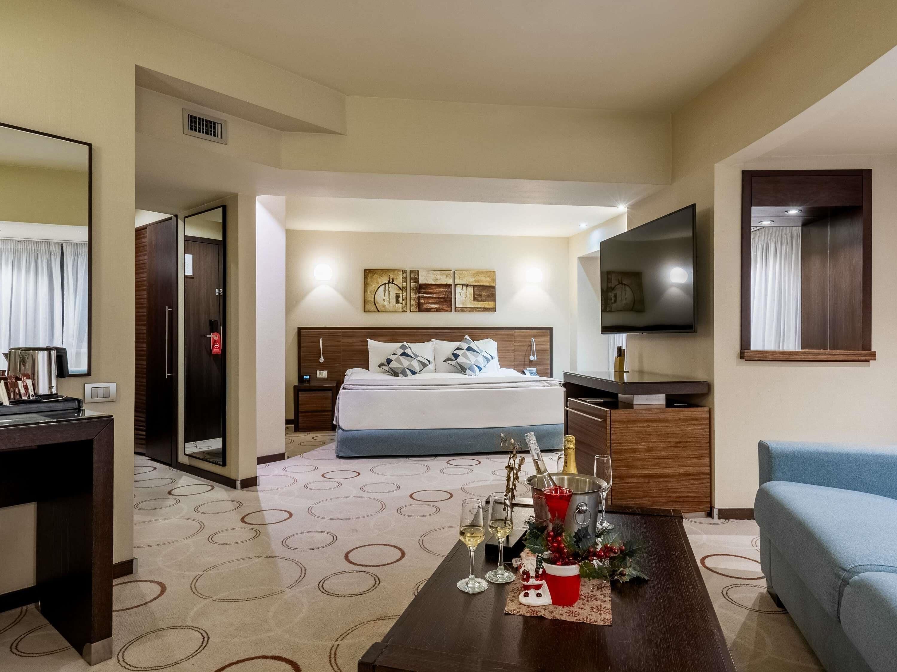 A hotel room with a bed, a TV, a desk, and a coffee machine.