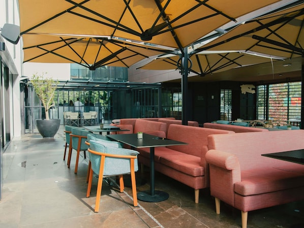 An indoor seating area with tables and sofas, large potted plants, and a modern architectural design.